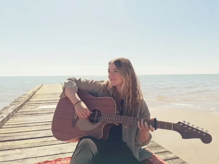 Johanna spielt Gitarre auf einem Holzsteg am Meer