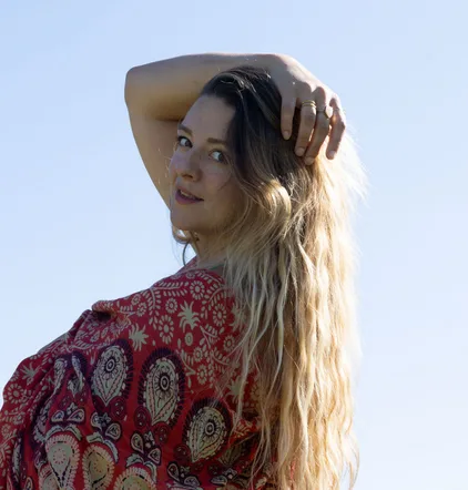 Johanna Schütz vor blauem Himmel, die Hand im Haar, Blick über die Schulter