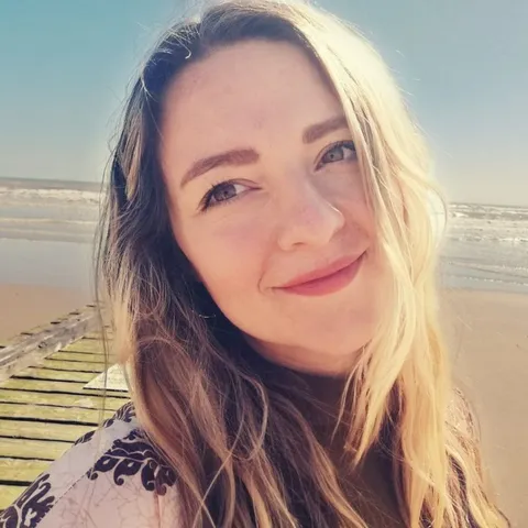 Johanna Schütz lächelnd am Strand, im Hintergrund ein Holzsteg und das Meer